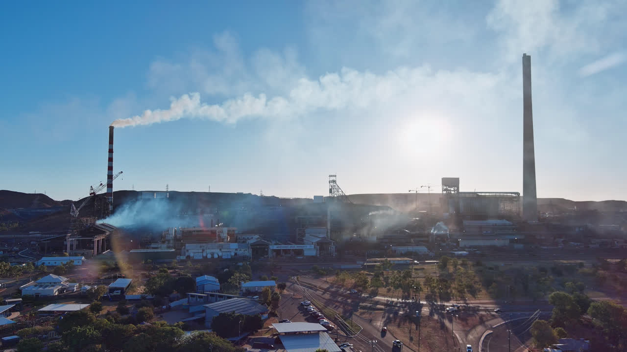 atrás, las minas del monte isa con columnas de humo de sus chimeneas con coches conduciendo y edificios en primer plano, monte isa, queensland, australia