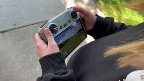 Little-kid-boy-or-girl-flying-drone-at-green-grass-wide-open-park-as-focus-is-on-small-child-tiny-hands-first-time-flight-on-beautiful-summer-day-with-blue-skies-and-clouds-on-screen---in-4K-60fps