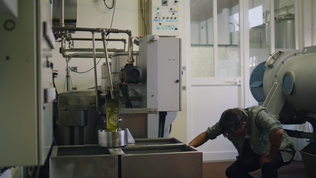 Serious man turning press machine at fabric closeup. Worker producing olive oil