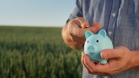 a man puts coins in a piggy bank, stands against the background of a field where wheat grows