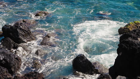 Static-close-up-shot-of-rough-ocean-waves-crushing-against-the-volcanic-rocky-coastline