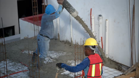 slow motion of two construction workers pouring applying fresh concrete from a boom pump onto the grid that will create the slab