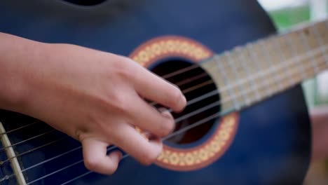 close up on boy finger picking strings of a blue acoustic guitar