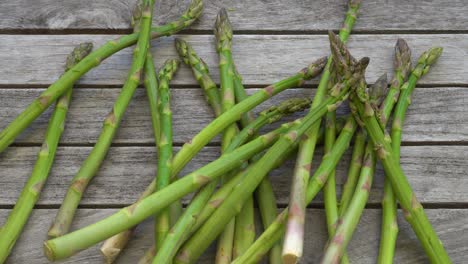 Aufnahmen-Von-Einem-Bund-Frischer,-Grüner-Spargel,-Der-Auf-Einen-Holztisch-Fällt