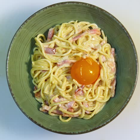 spaghetti carbonara. carbonara is made with eggs, bacon, pepper and grated pecorino cheese. chef puts egg yolk to the dish