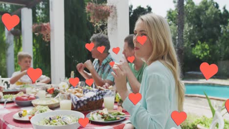 Animation-of-hearts-over-caucasian-family-eating-in-garden