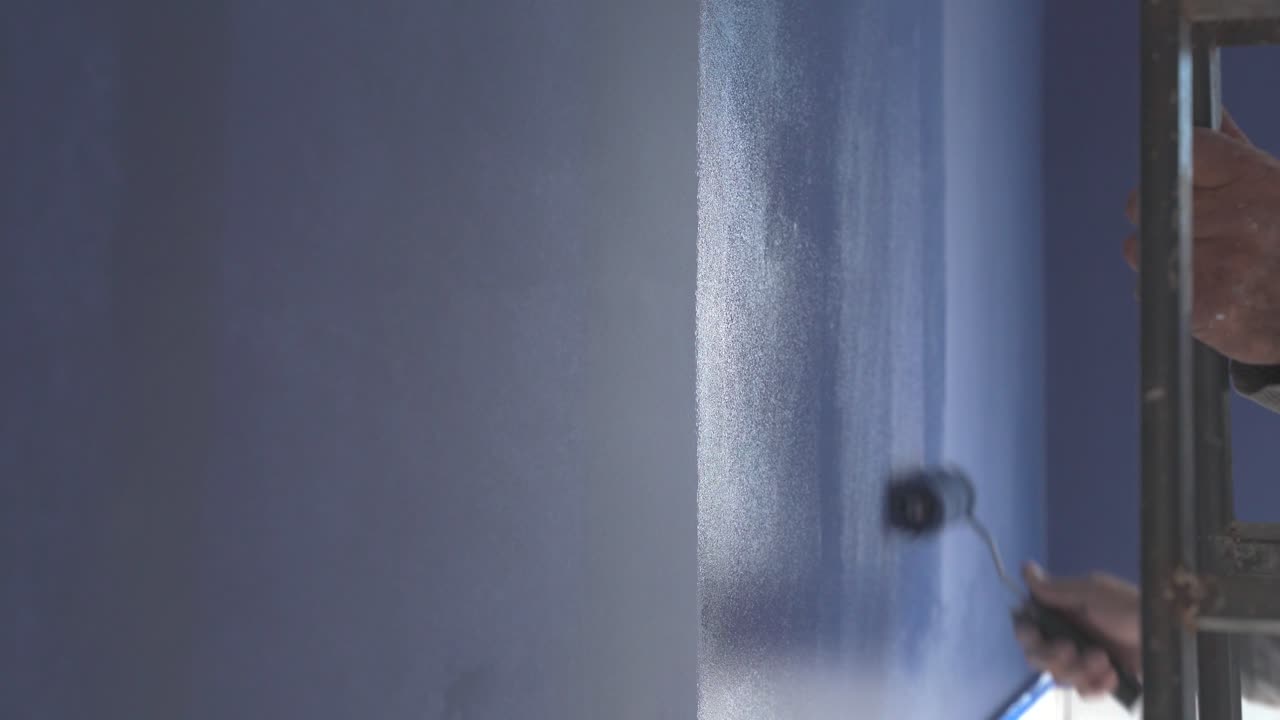 Primer plano de una mano humana pintando una pared en una habitación con un rodillo pequeño de color azul