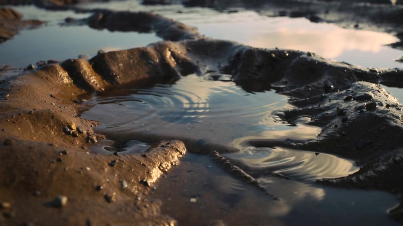 Mostrando una pozzanghera poco profonda che reagisce a una piccola perturbazione nella piana di fango, con increspature che si diffondono in un vortice.