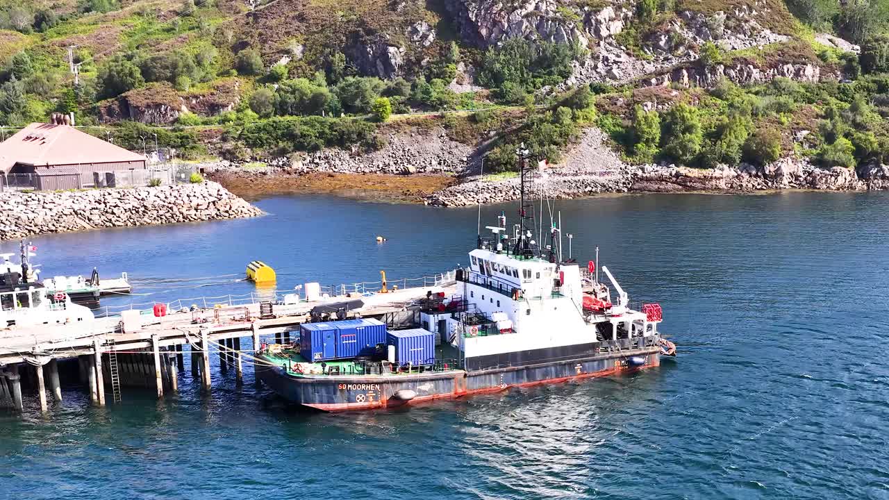 A cargo vessel slowly approaches and docks at a sunny, scenic harbor in Dundee, Scotland