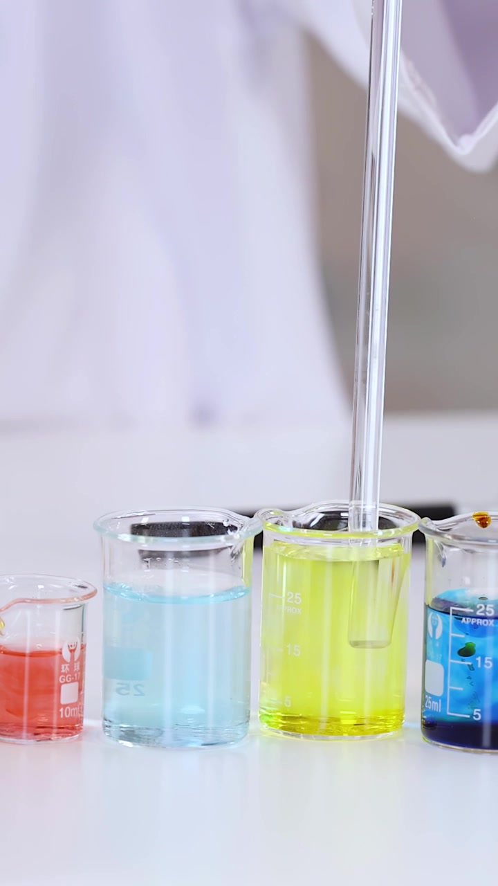 Primo piano di uno scienziato in camice bianco da laboratorio che mescola liquidi colorati usando una pipetta.