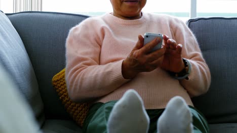 Senior-woman-using-mobile-phone-in-living-room