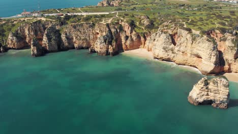 algarve limestone coastline barring emerald-green mediterranean sea - aerial high fly-over push in shot