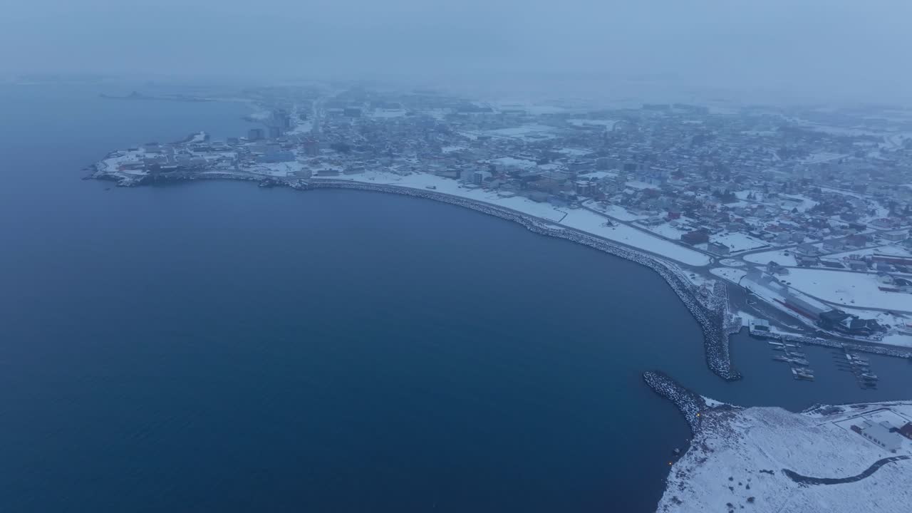 Langsomt luftpanoramabilde av snødekt kystlinje, hav og by i Keflavik, Island, om vinteren.