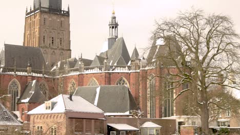 slow pan showing the remains of the medieval city wall revealing the drogenapstoren rising above winter barren trees part of the cityscape of hanseatic city zutphen, the netherlands, covered in snow