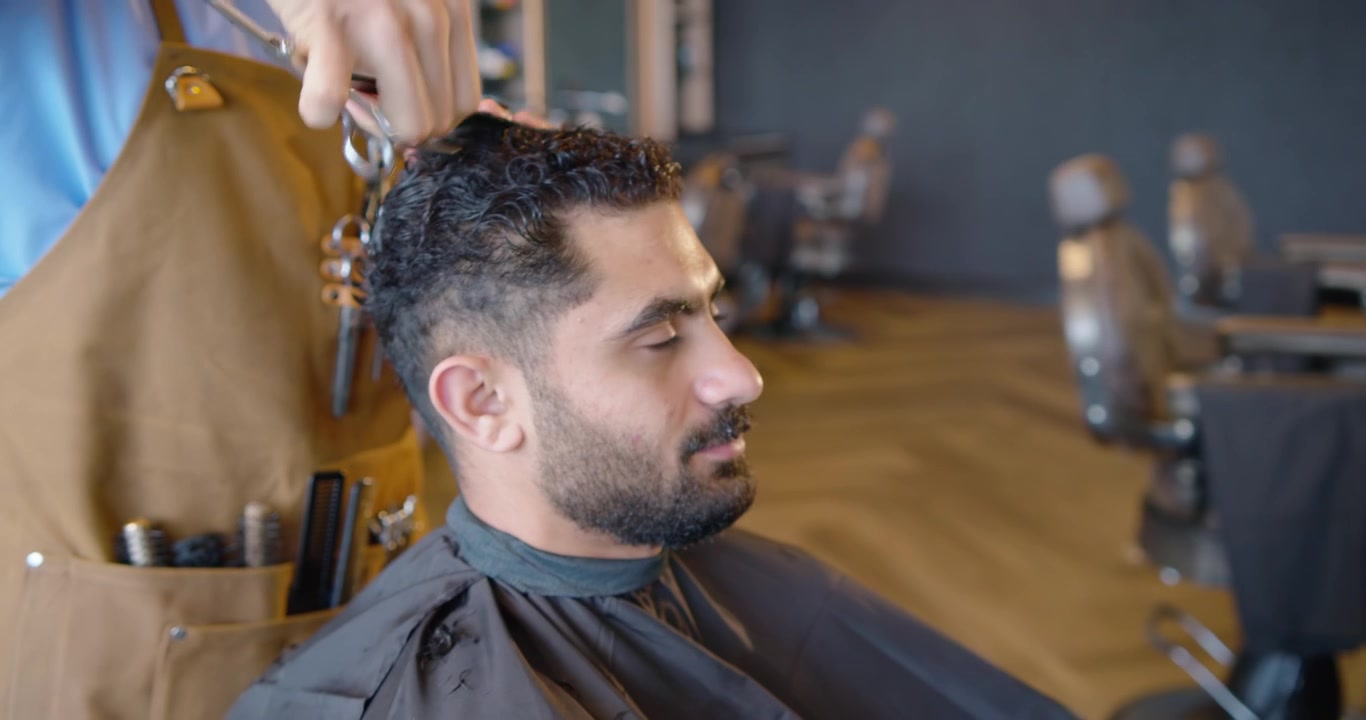 Mandlig frisør inddeler mandlig kundes hår med kam og klemme, klipper for at forkorte toppen i salon.
