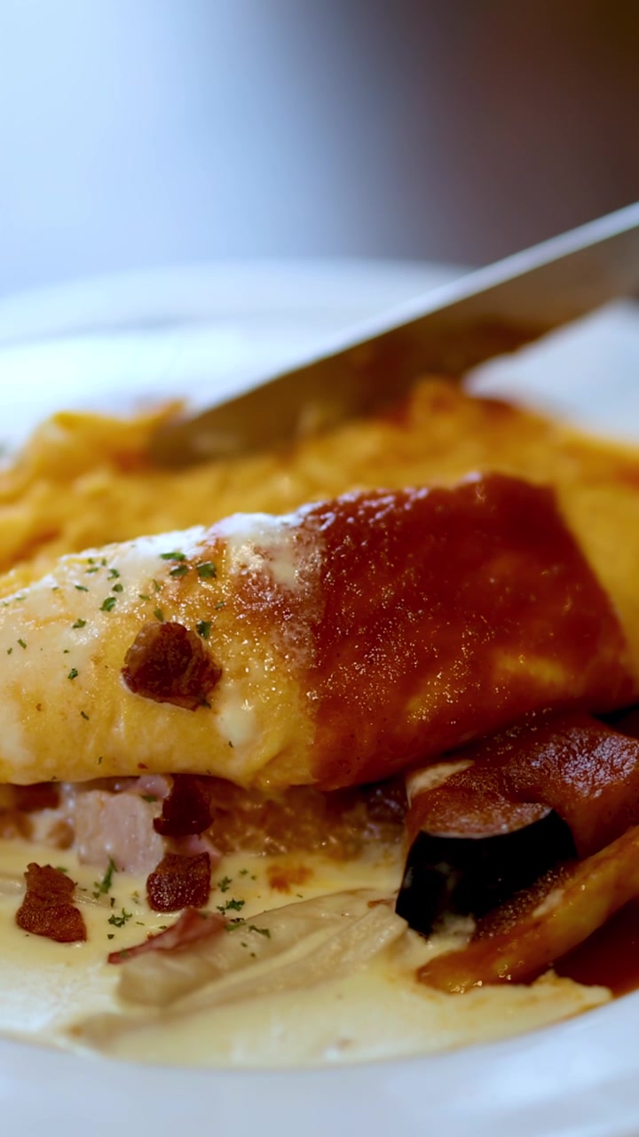 Una mano taglia omurice giapponese con un coltello, rivelando il ripieno di riso, in un ambiente di ristorante illuminato delicatamente.