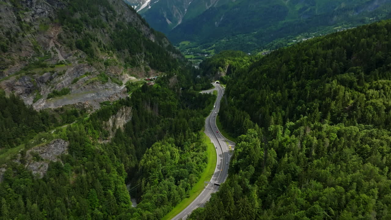 Aerial view tilting backwards over a road, revealing snowy alpines of Chamonix