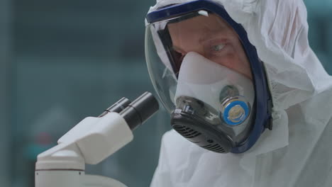 microbiologist-is-exploring-dangerous-bacteria-by-microscope-in-laboratory-protecting-himself-by-overall-and-mask-with-respirator-closeup-of-human-face