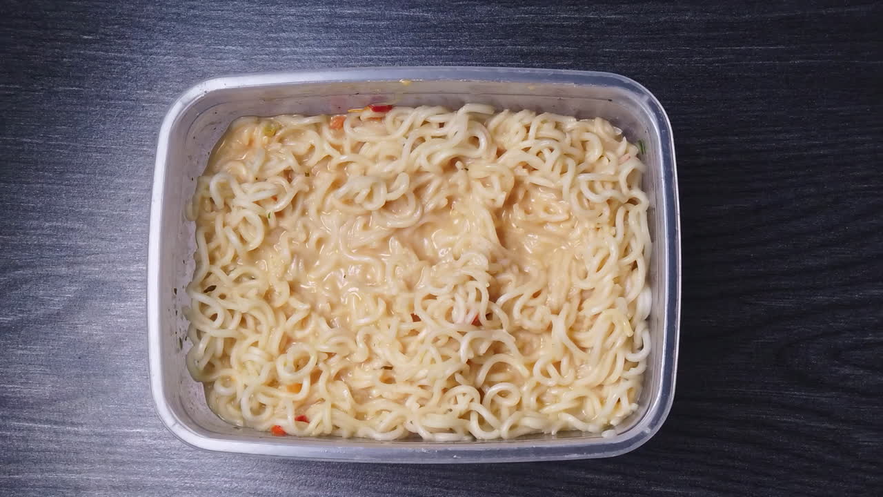 Overhead shot of falling pieces of the sausage in noodles with sauce on wooden table in the kitchen