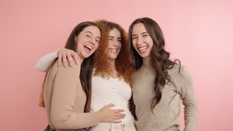 cheerful young women hugging in pink studio
