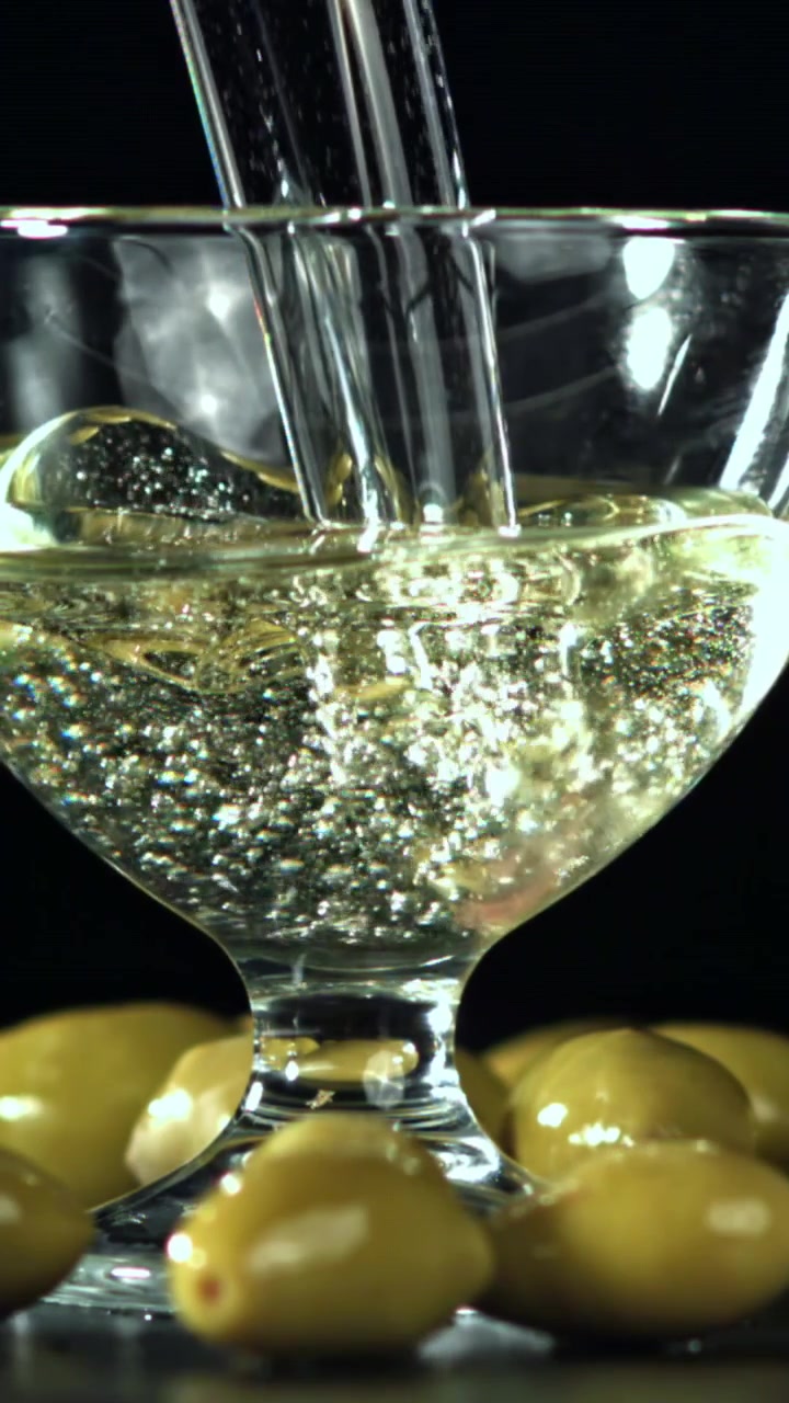 Versamento al rallentatore di Martini in un bicchiere con olive