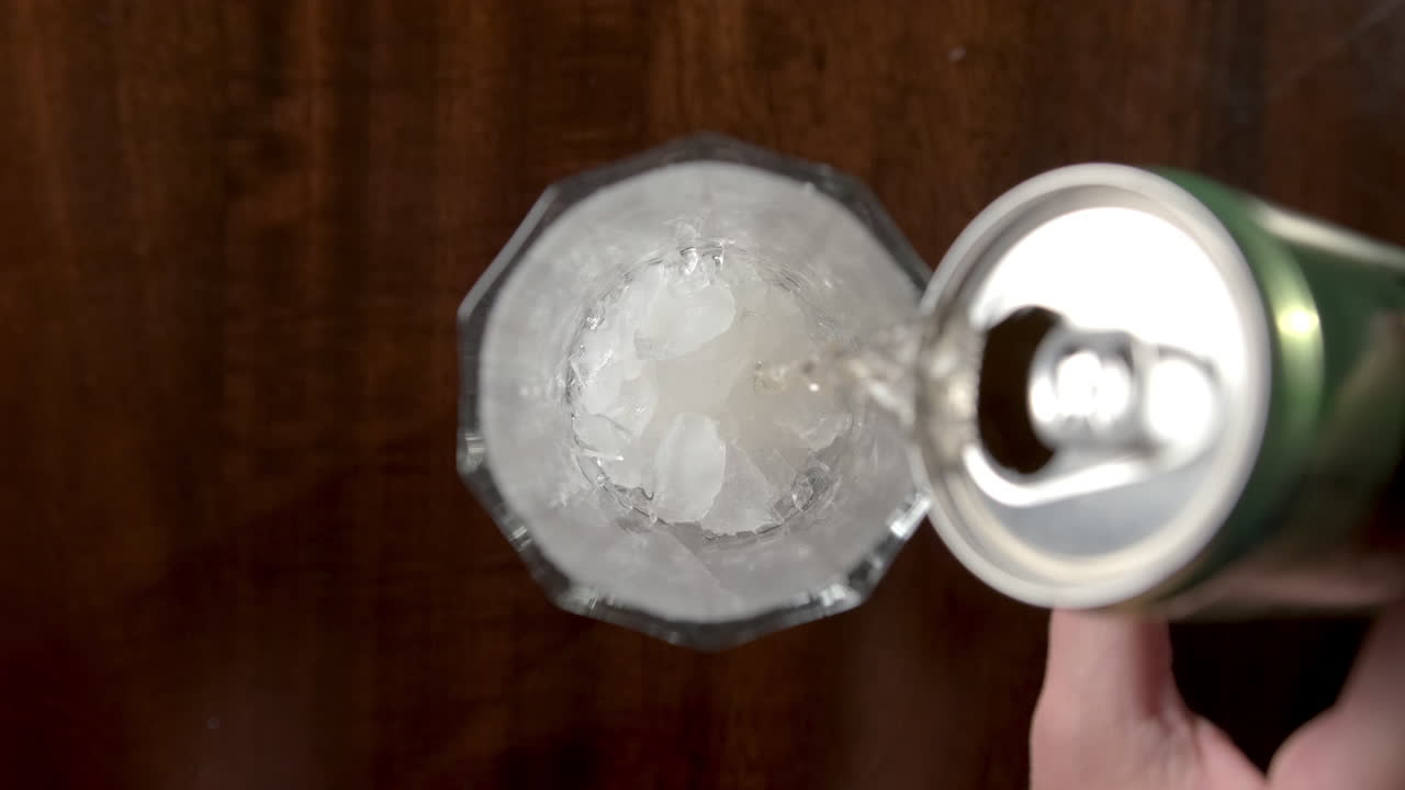 mano femenina vertiendo cerveza en un vaso con cubitos de hielo