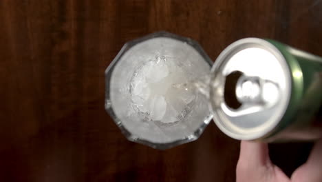mano femenina vertiendo cerveza en un vaso con cubitos de hielo