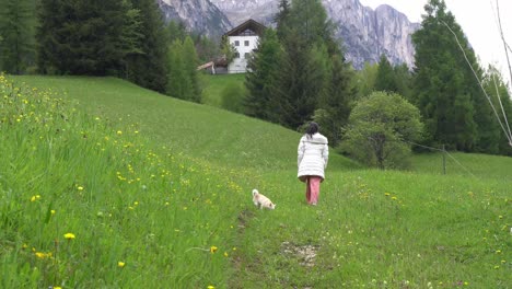 woman and her pet dog walking on grassy field in rural italy - wide shot