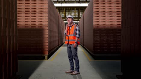 full body side view of asian male engineer with safety helmet thinking and looking around then raising his index finger while standing with red brick packed in stacks are stored
