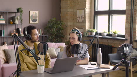 Cuc-Woman-And-Man-With-Headphones-Are-Sitting-At-Table-With-Microphone-And-Laptop-While-Recording-A-Podcast