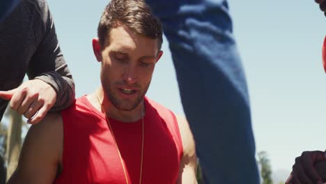 Diverse-fit-group-discussing-performance-with-male-trainer-at-obstacle-course-in-the-sun