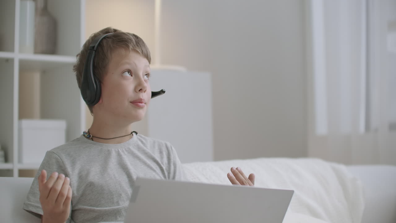 preschooler boy is drawing and chatting online with friend or parent by laptop with headphones sitting at home