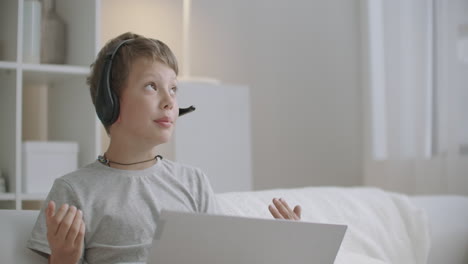 preschooler boy is drawing and chatting online with friend or parent by laptop with headphones sitting at home