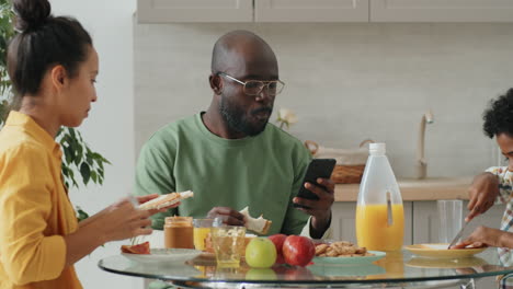 african american man using smartphone on breakfast with family at home