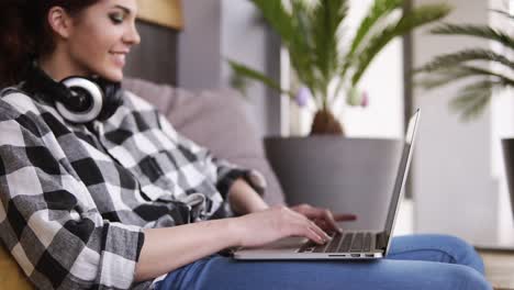 aiming footage of the laptop opening by a smiling young girl with headphones. the girl begins communication on the internet. typing. has a rest on a couch