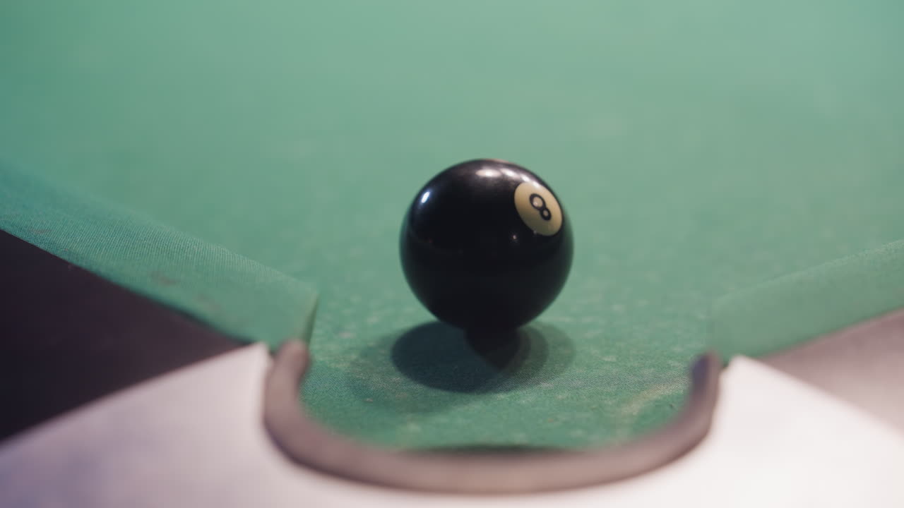 vista frontal de la pelota de billar negra rodando hacia el bolsillo de la piscina después de ser golpeada por la pelota blanca en la mesa de fieltro verde. primer plano captura el movimiento, la precisión y la dinámica del juego de billar