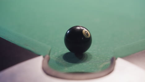 front view of black billiard ball rolling toward pool pocket after being struck by white cue ball on green felt table. close-up captures motion, precision, and dynamics of billiards gameplay