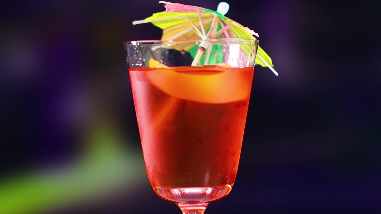 Una bebida roja vibrante en un vaso con una sombrilla decorativa, sobre un fondo de luces difuminadas.
