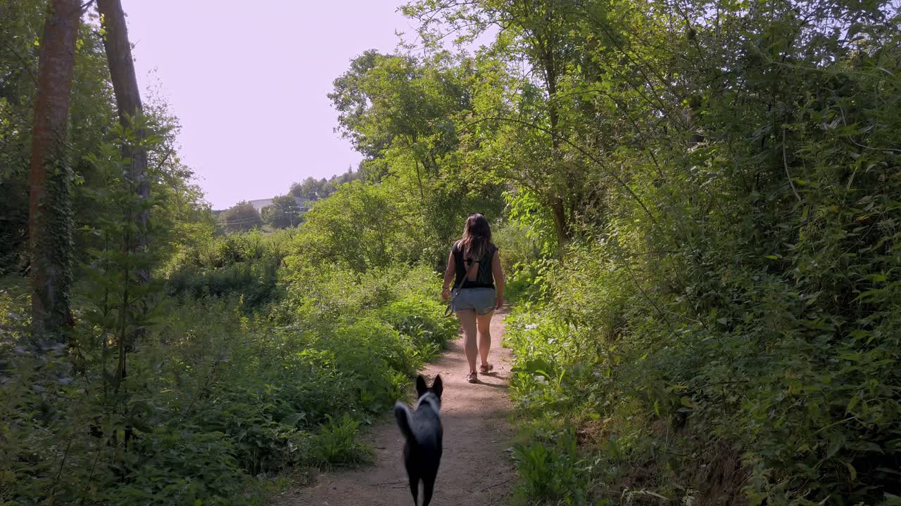 mujer joven caminando por el campo perseguida por su perro blanco y negro