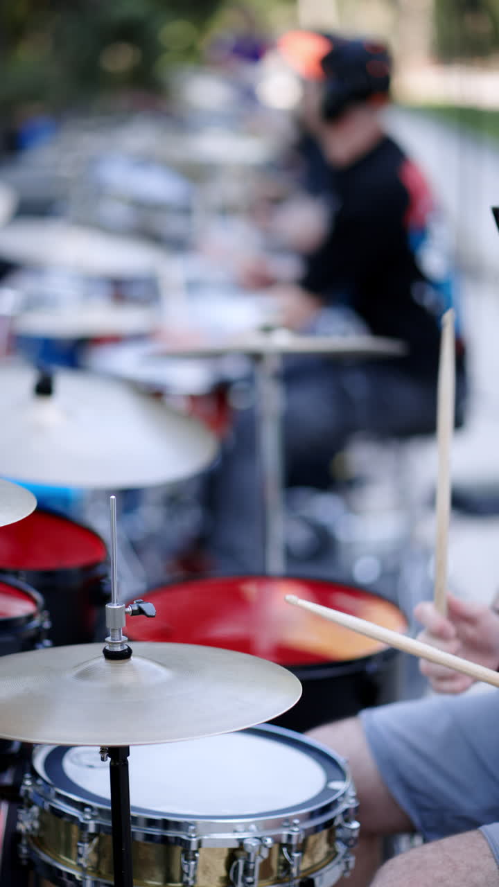 Close up of man playing red drums with a band outside. Vertical