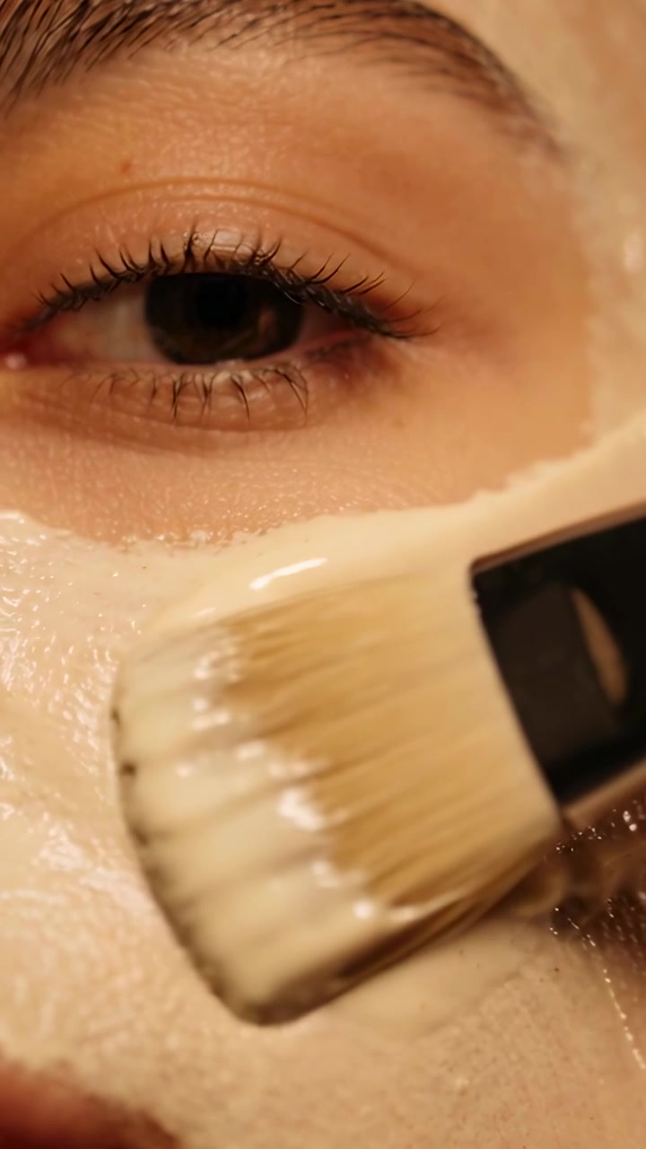 Video verticale: Partendo da una macchia di crema, un pennello piatto trascina la crema levigando la guancia davanti alla toeletta.