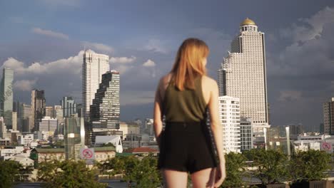 a young woman points out towards the city skyline in central bangkok