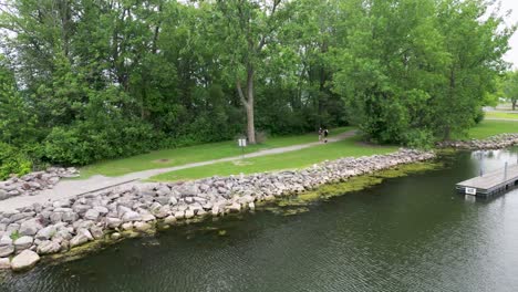 Drone-shot-of-a-lakeside-path,-bordered-by-lush-trees-and-rocks,-with-walkers-enjoying-the-serene-scenery