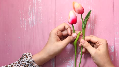 hands arranging artificial tulips on a pink wooden background