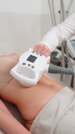 cosmetologist performs lpg body contouring therapy on woman lying in clinic during slimming session