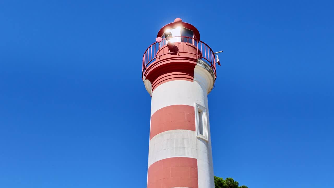Red and white striped lighthouse with clear blue sky in background, sun glints off lantern room, La Rochelle, France