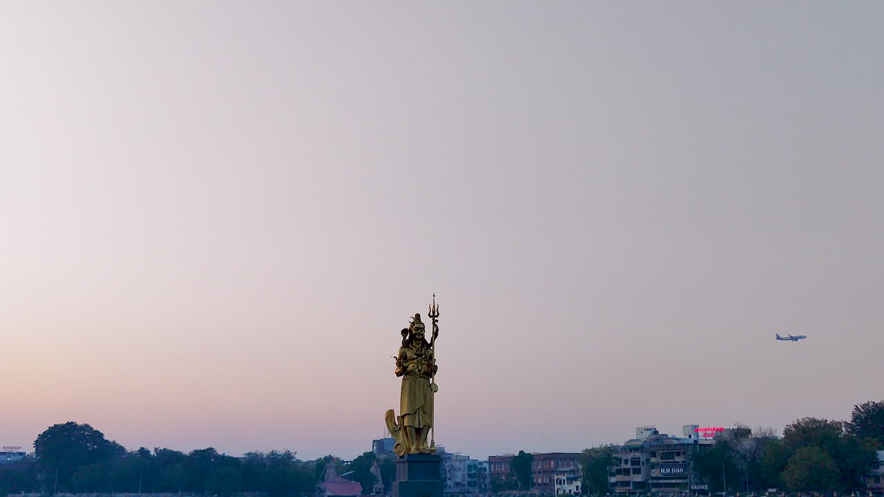 he aquí el esplendor de una hermosa vista frontal de la inmensa estatua dorada del señor shiva en el lago sursagar en vadodara al anochecer, con un avión volando bajo pasando en el fondo