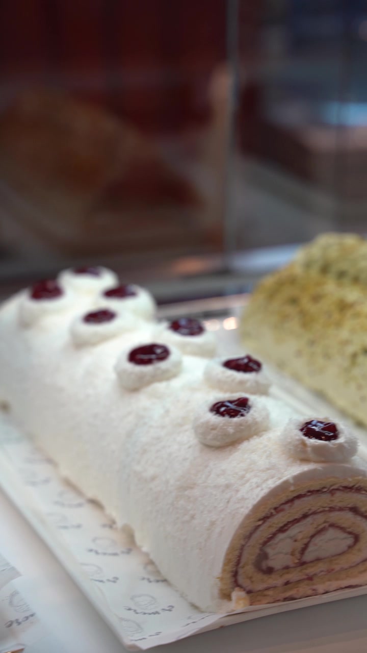 Bir kafe penceresinde fıstık kaplı bir dilim ve orman meyveli reçelli beyaz kremalı bir rulo pasta içeren, iştah açıcı gurme pandispanya rulo kek görünümü.