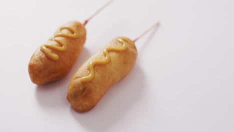 video of corn dogs with mustard on a white surface