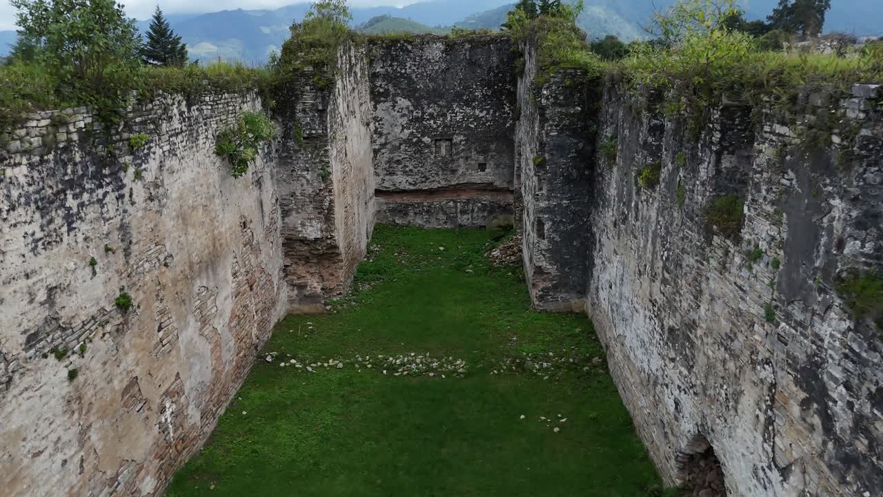 A dolly shot moves backward between ancient stone walls with nature growing all around.